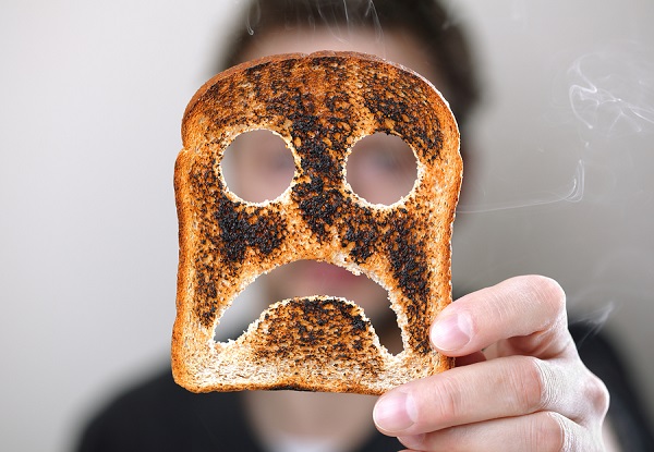 Man holding up a burnt slice of toast with an unhappy smiley con